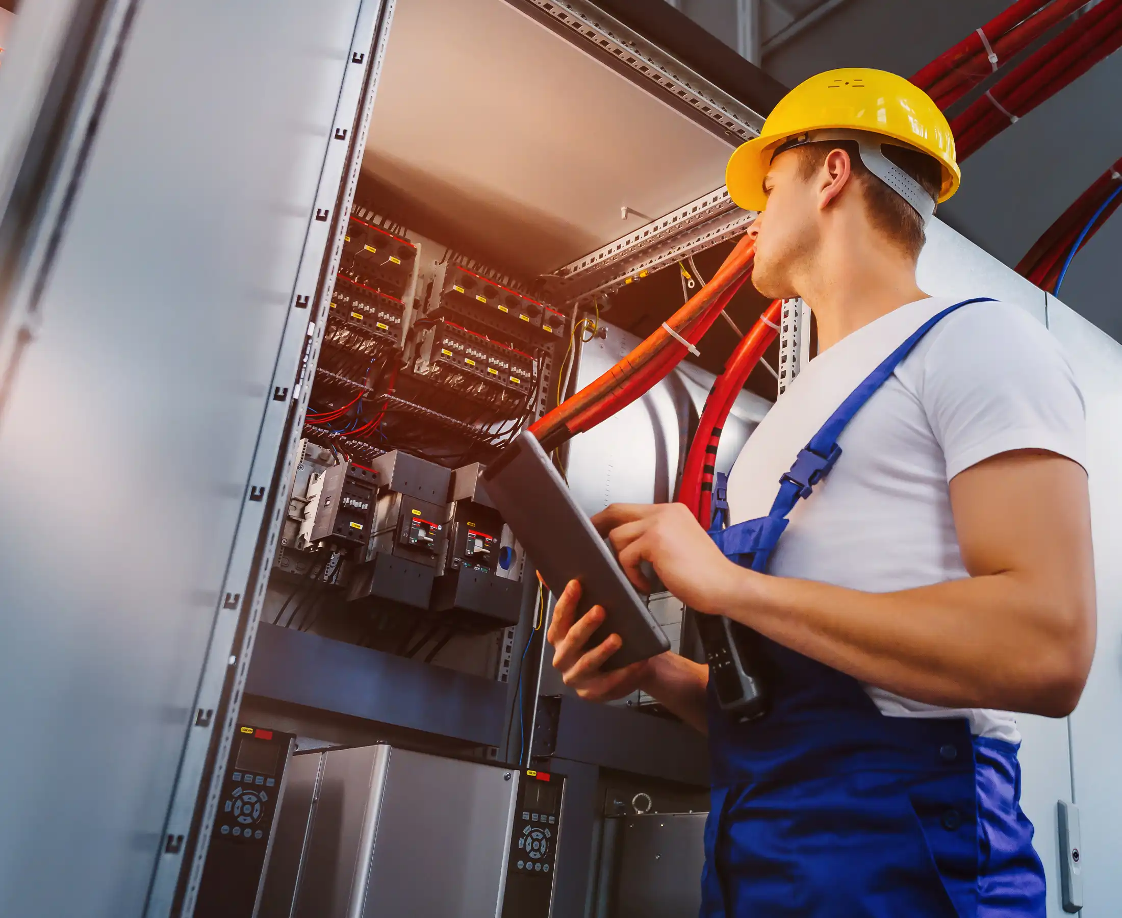 electrician works with a tablet standing near an industrial fuse board cabinet